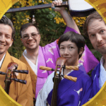 Four people in colorful kimonos smile outdoors, holding traditional Japanese string instruments, with green foliage and yellow leaves in the background.