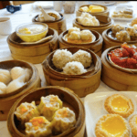 A table filled with assorted dim sum in bamboo steamers, including dumplings, rice balls, egg tarts, and various bite-sized dishes, ready to be served.