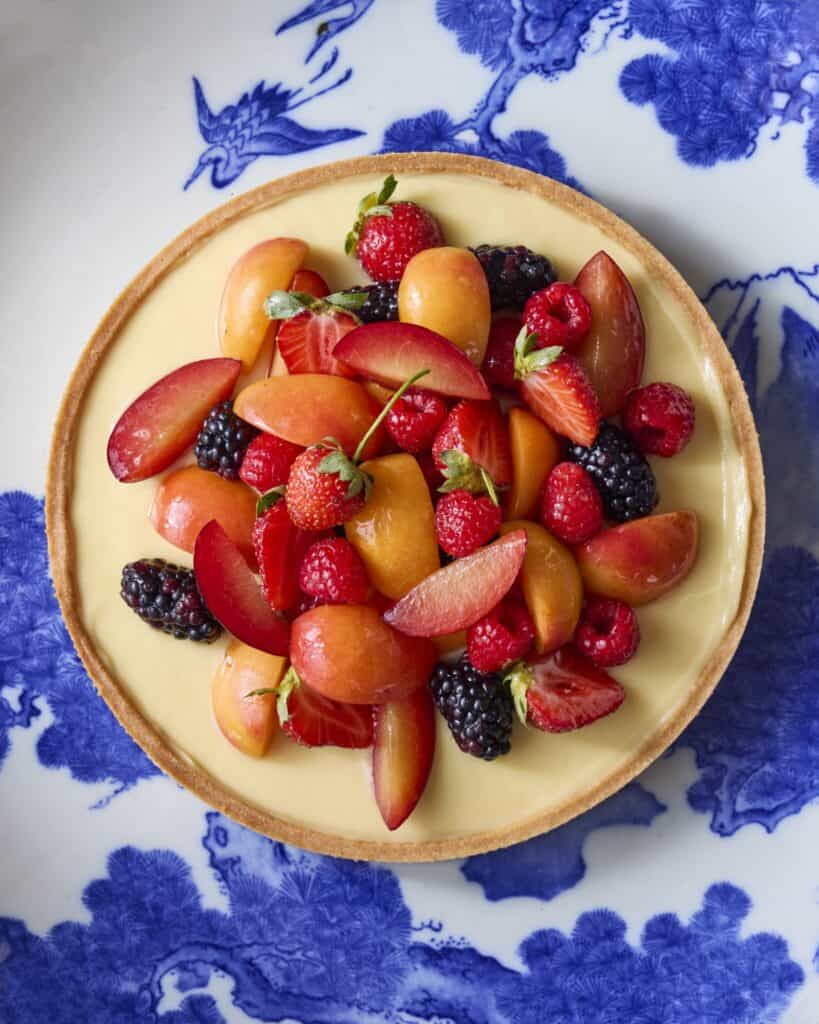 A tart topped with sliced plums, strawberries, blackberries, and apricots sits on a blue and white patterned plate.