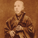 Sepia-toned photo of an elderly person in traditional Japanese clothing, holding a bamboo flute with both hands, looking slightly to the side.