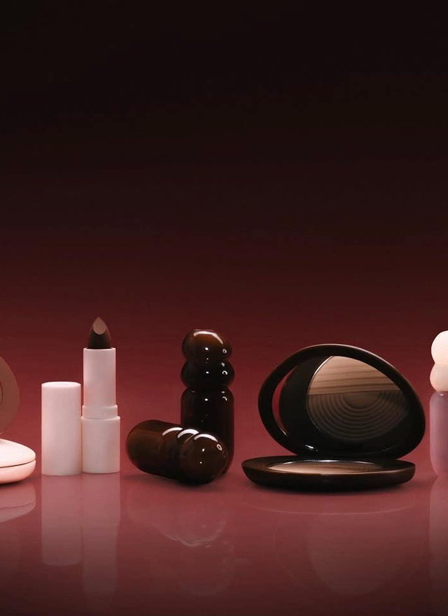 A set of various makeup products including lipstick, compacts, and bottles, arranged neatly against a gradient burgundy background.