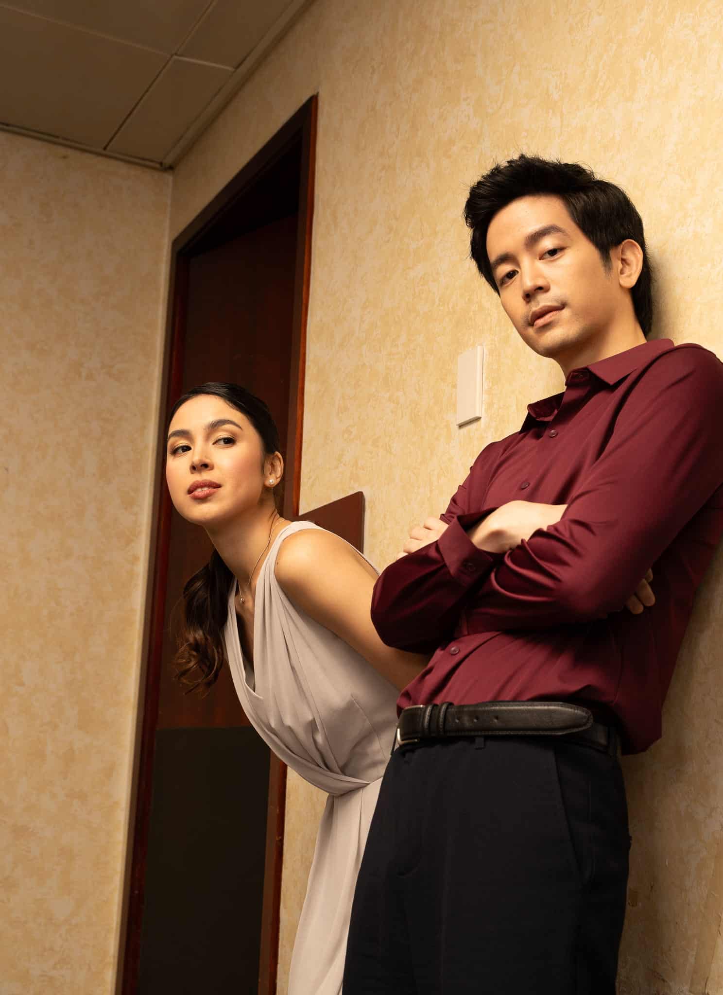 A man with his arms crossed stands next to a woman, both looking toward the camera.