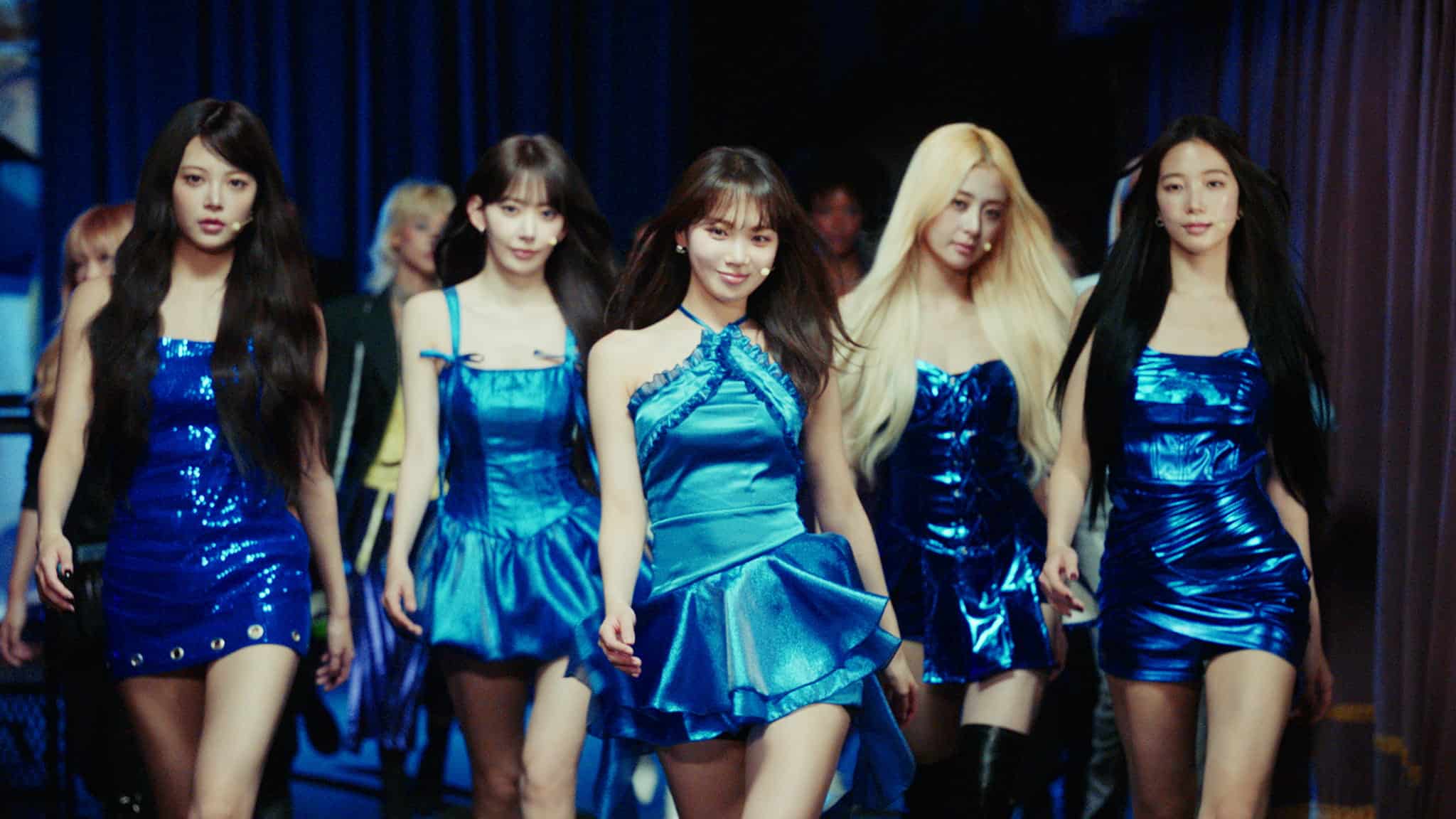 Five women wearing metallic blue dresses walking together on a stage.
