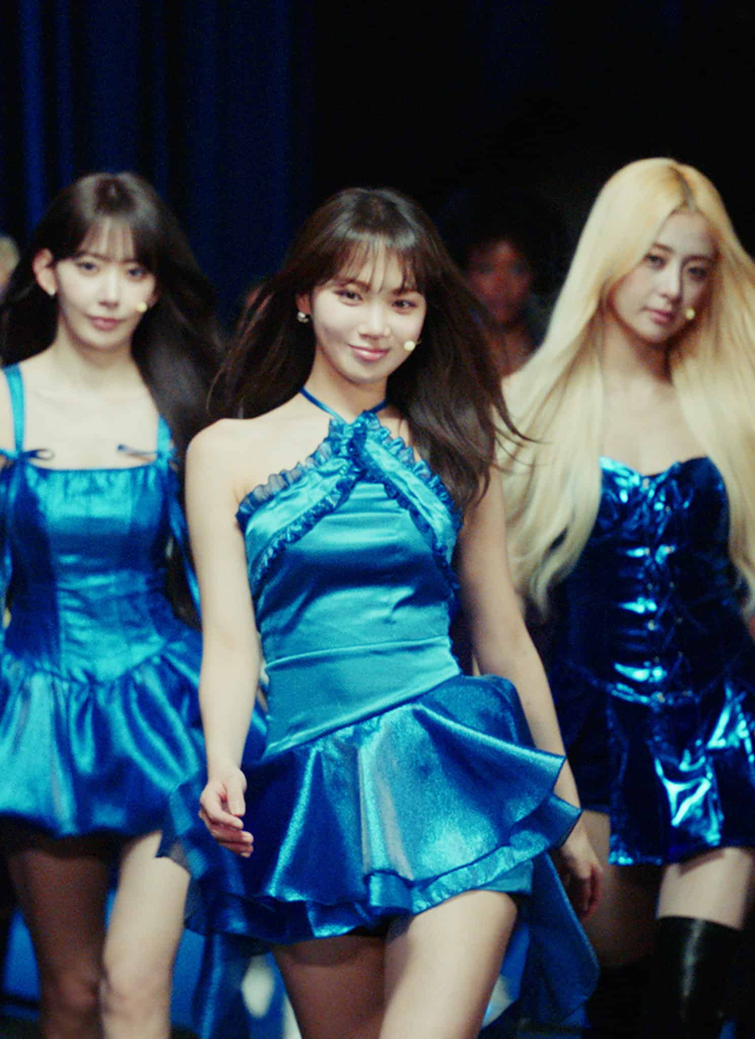 Five women wearing metallic blue dresses walking together on a stage.