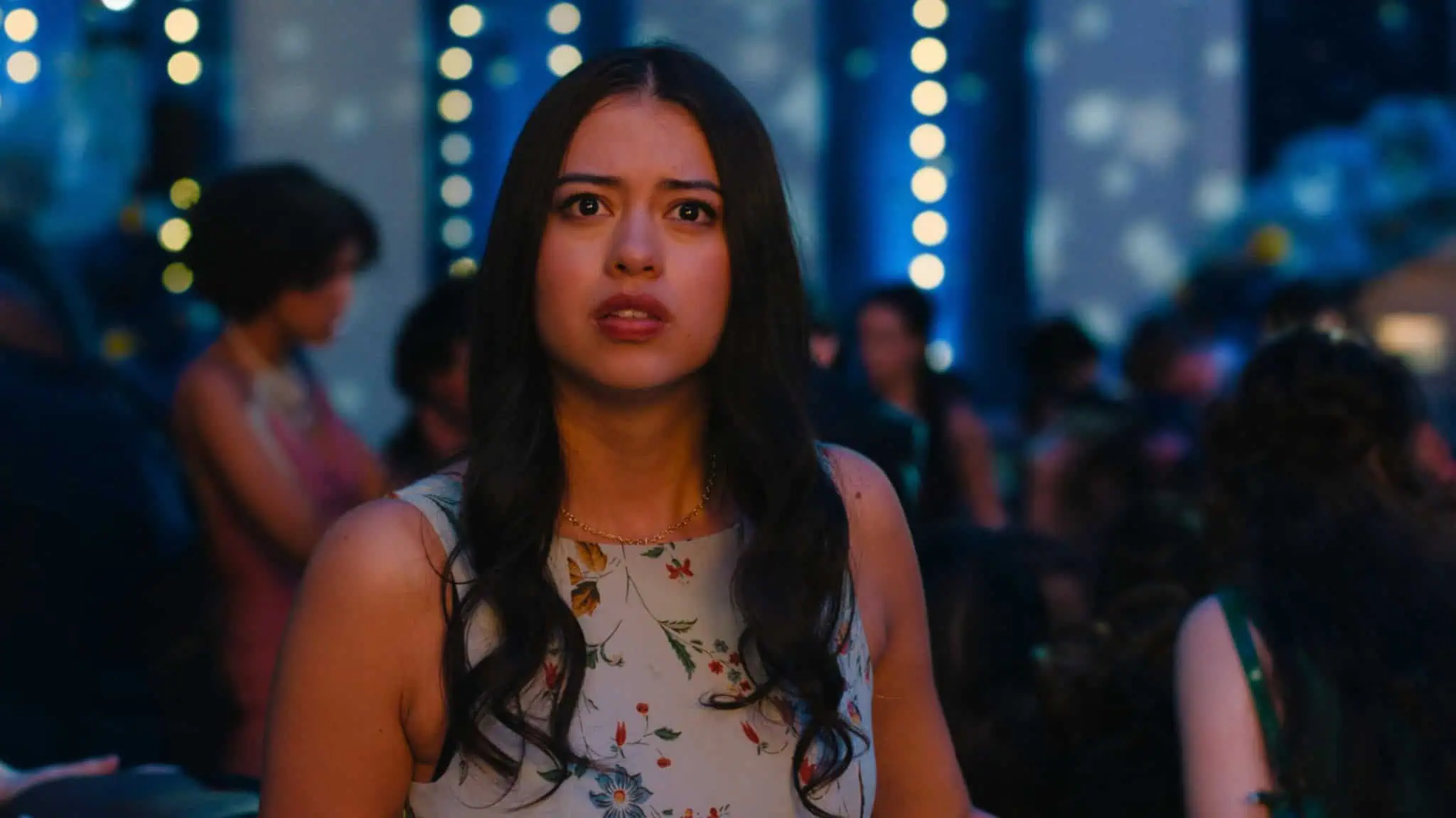 A young woman with a concerned expression stands in a crowd under blue string lights.