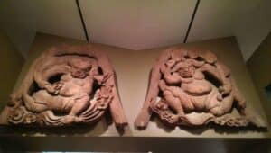 two carved wooden figures, holding a bag of wind and beating thunder drums