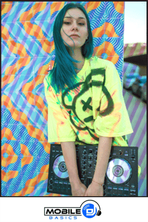 A woman with blue hair wearing a neon yellow shirt stands in front of a colorful patterned background, holding a DJ controller—showcasing what should a mobile DJ wear to stand out at any event.