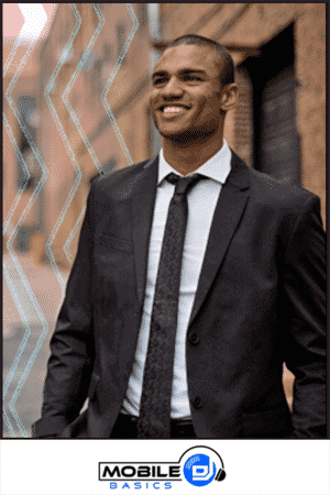 A man in a black suit and tie stands outdoors, smiling—showcasing what should a mobile DJ wear for a polished, professional look. The logo at the bottom reads "Mobile DJ Basics.