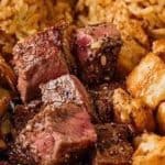 A plate with grilled steak cubes, chicken pieces topped with sesame seeds, sautéed vegetables, and a serving of fried rice.