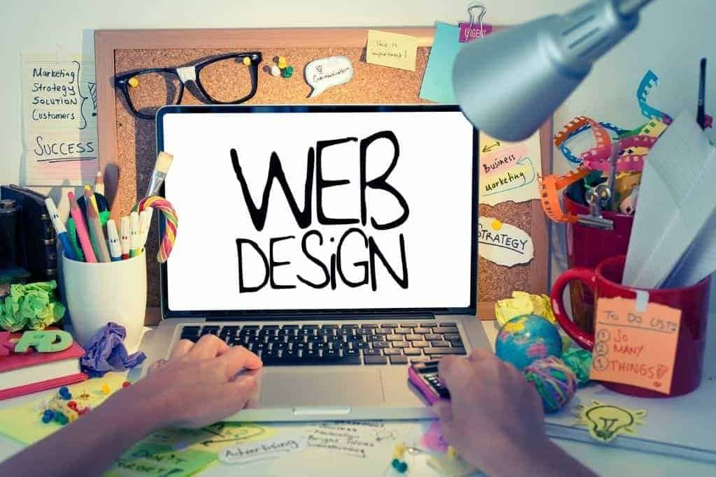 Messy table with laptop and the words web design on the main screen