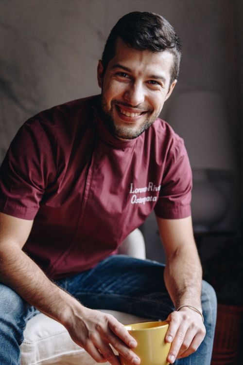 Foto di Lorenzo seduto in poltrona, mentre sorridente regge in mano una tazza di tè.