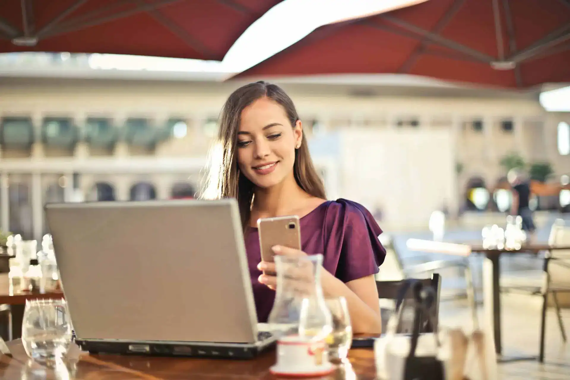 Pretty lady holding her phone in front of a laptop in a restaurant