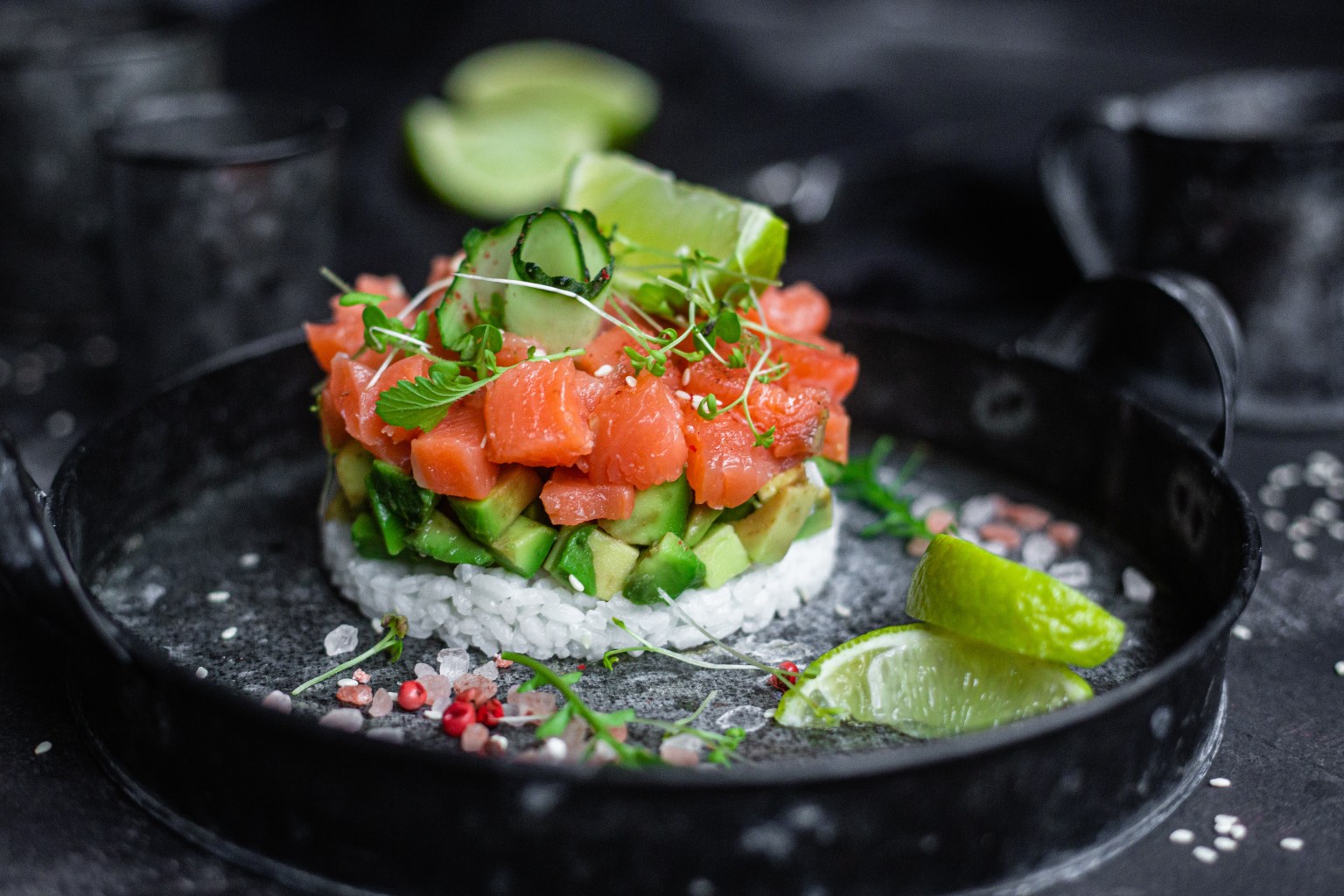 A plated round of salmon tartare with cucumber and microgreens on dark stone