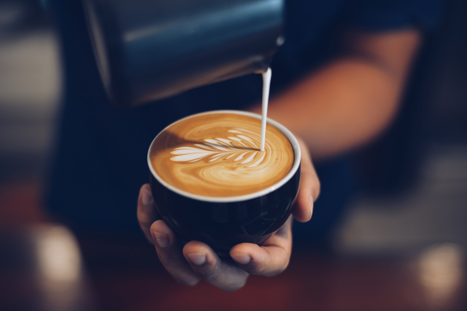 Hands pouring steamed milk into a cappuccino to form leaf latte art