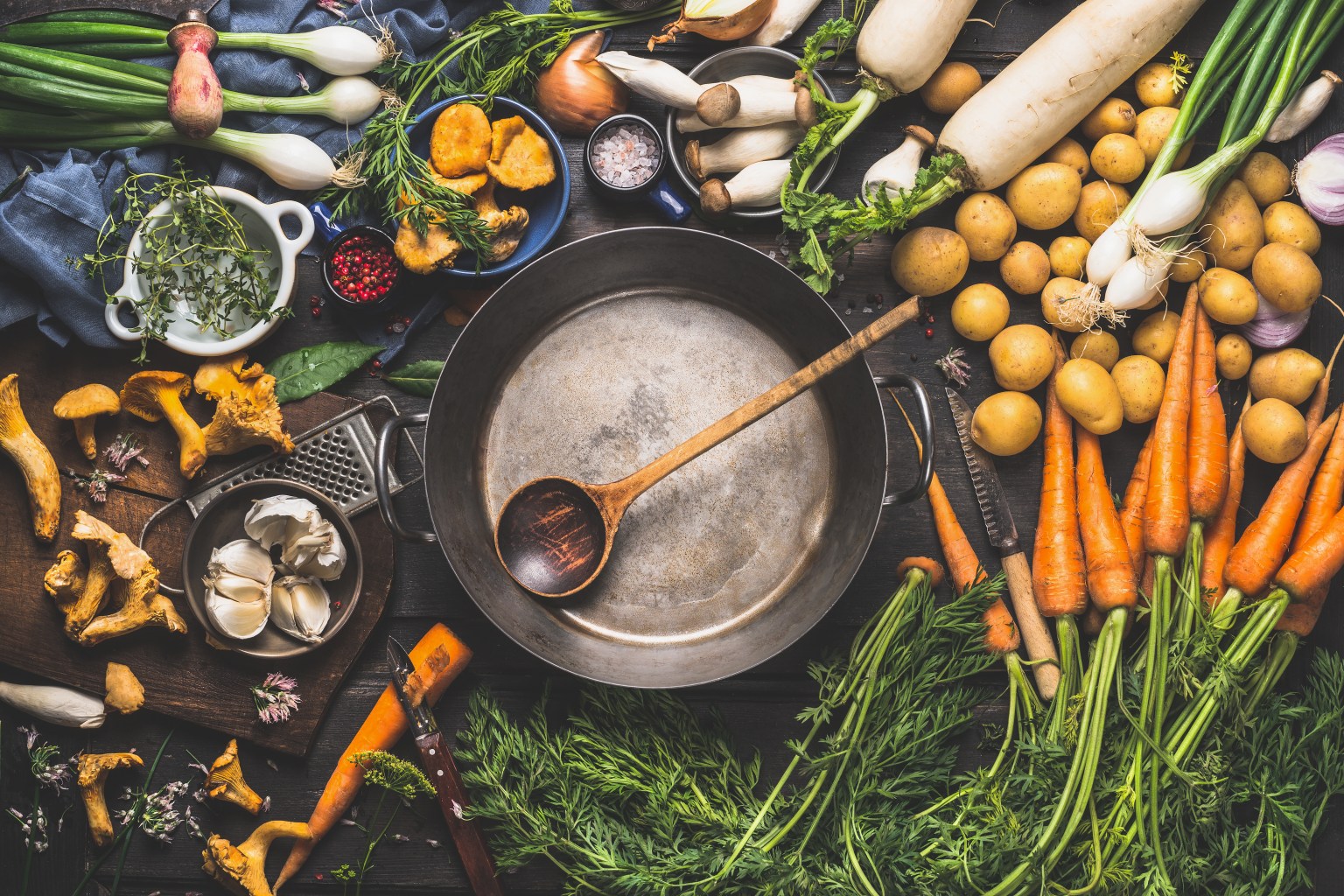 Fresh vegetables and cooking ingredients around a pot on a kitchen table