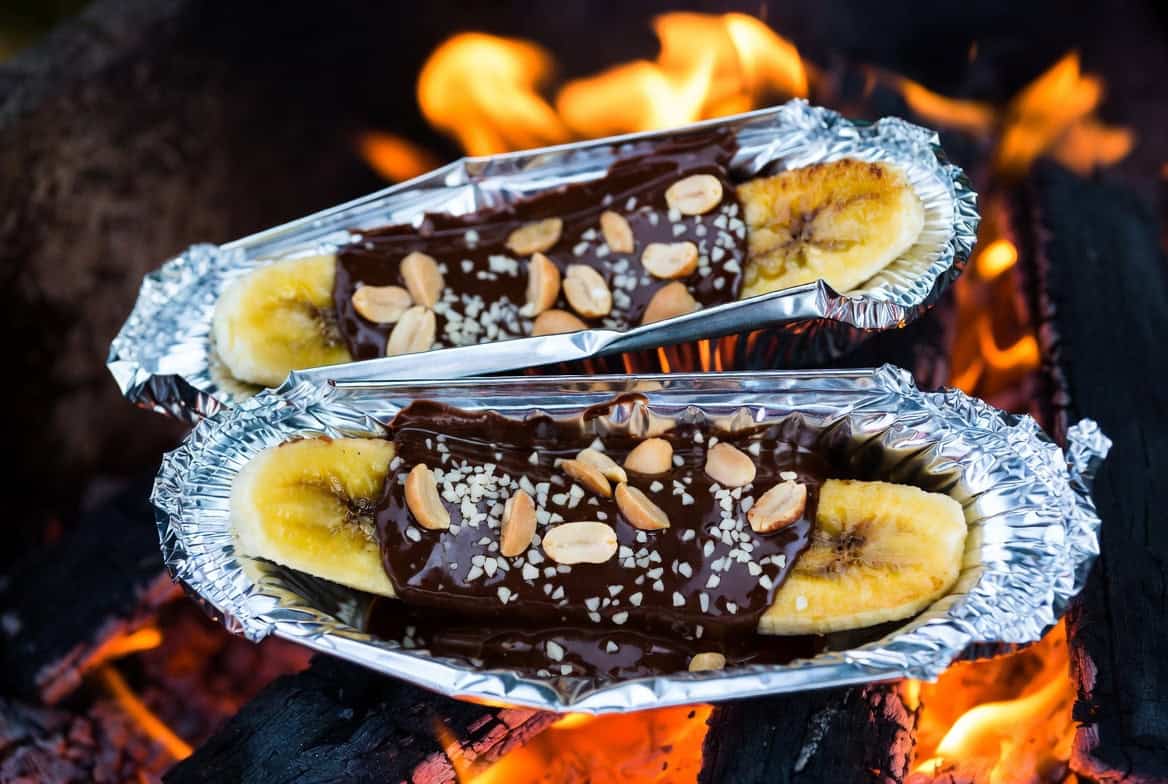 Foil banana boats with melted dark chocolate and salted peanuts over campfire