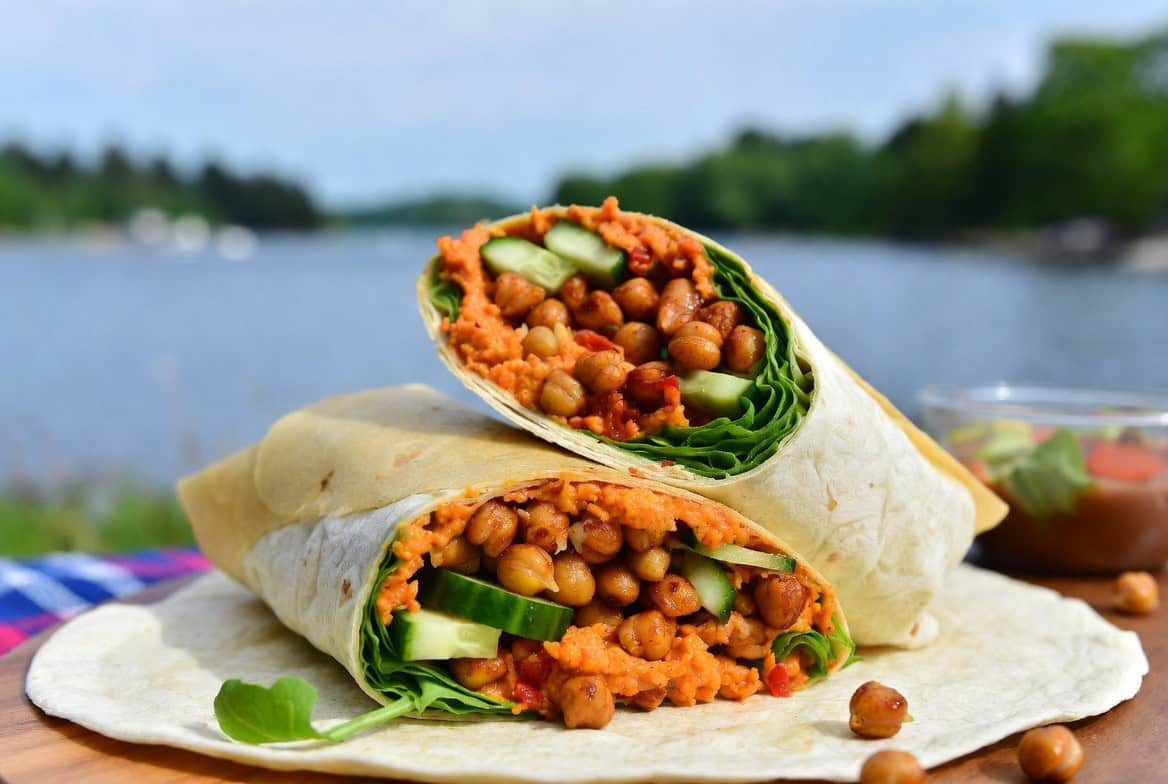 Red pepper hummus wraps with crunchy chickpeas cut in half by a lake