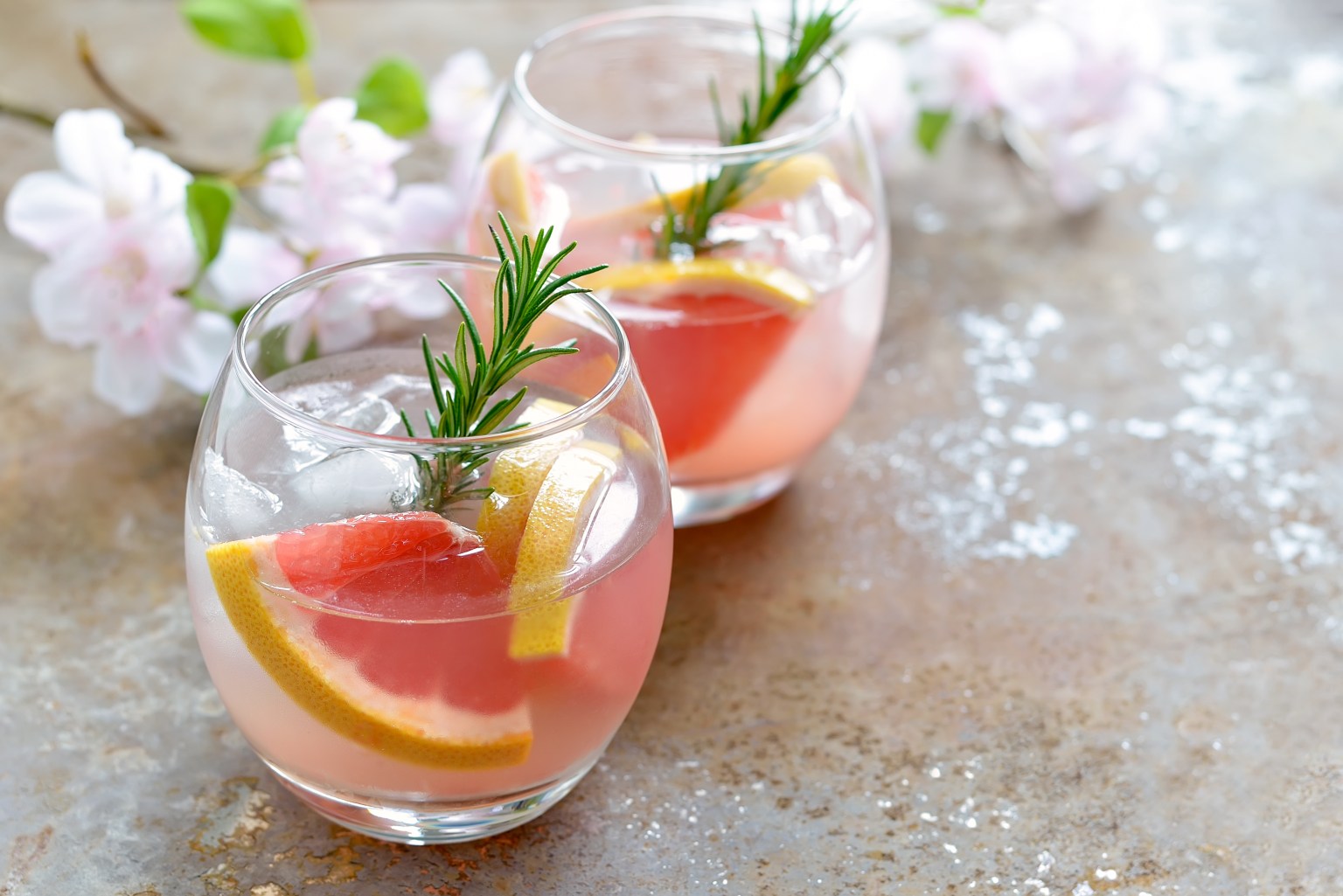 Two pale grapefruit cocktails with rosemary sprigs and citrus peel on crushed ice