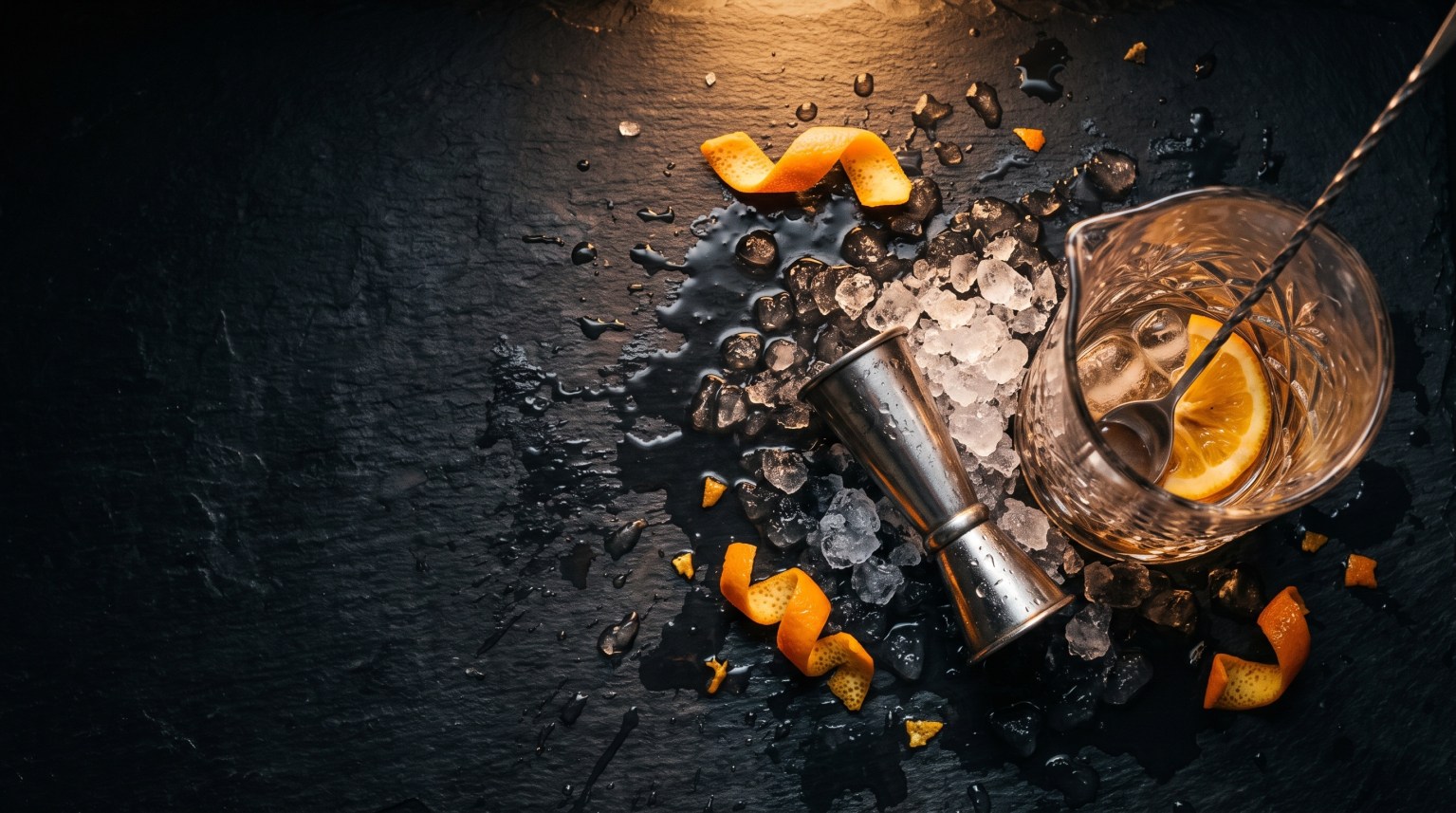 A coupe on a dark counter with crushed ice and curled orange peel scattered around