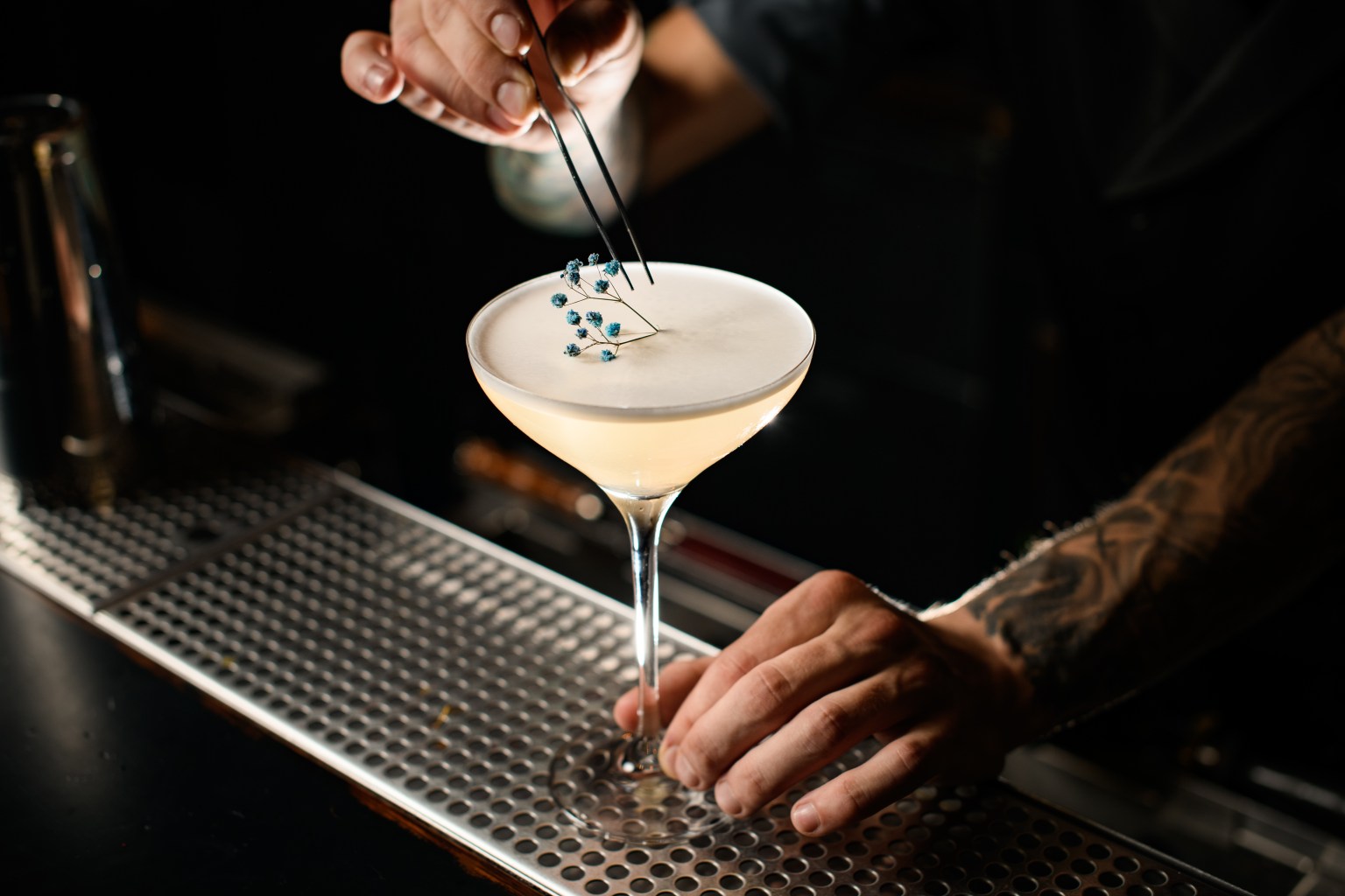 A bartender garnishing a foam-topped cocktail in a stemmed glass