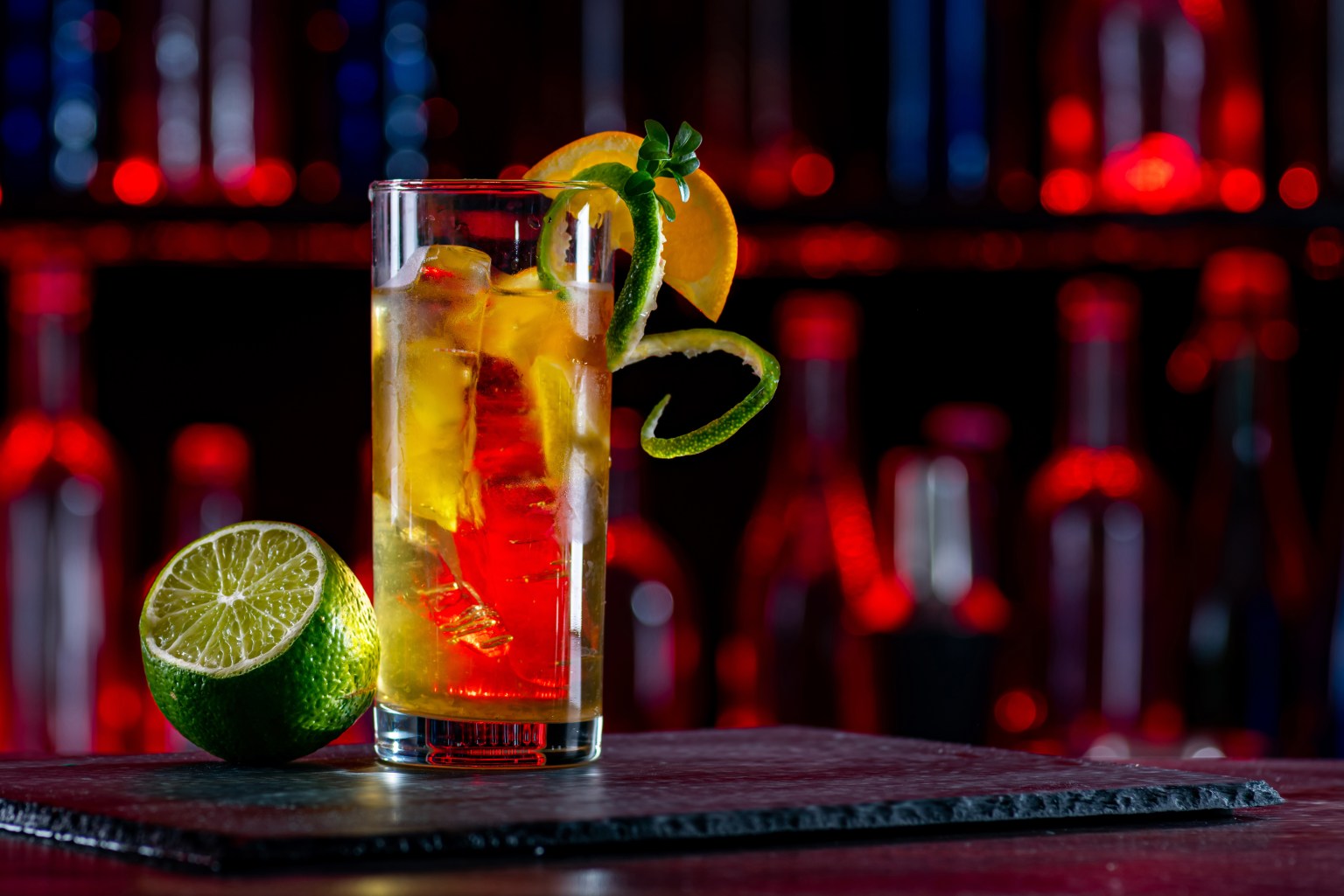 Two tall drinks with lemon twists glowing against red and blue bar neon