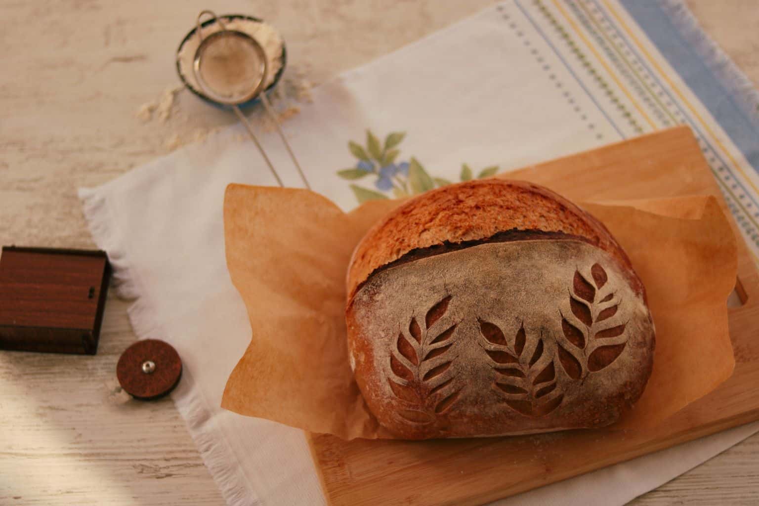 A deeply browned sourdough loaf with decorative scoring on a wooden board, showing the crust and finished shape clearly