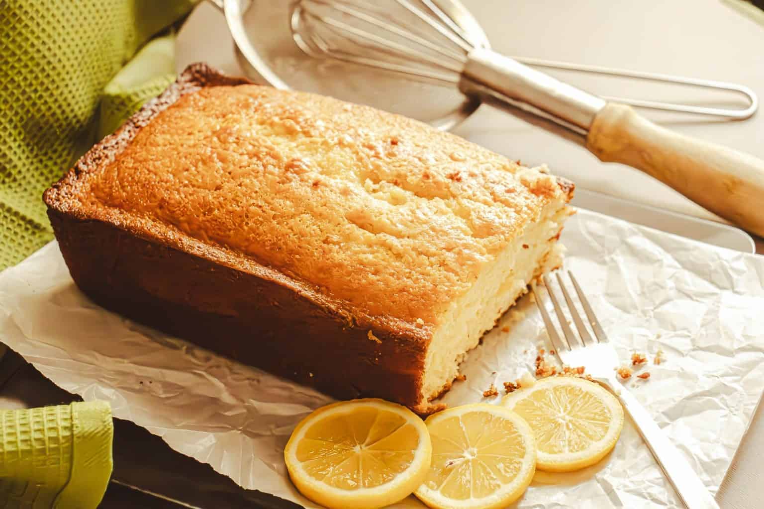 Plain golden lemon cake on baking paper with fresh lemon slices