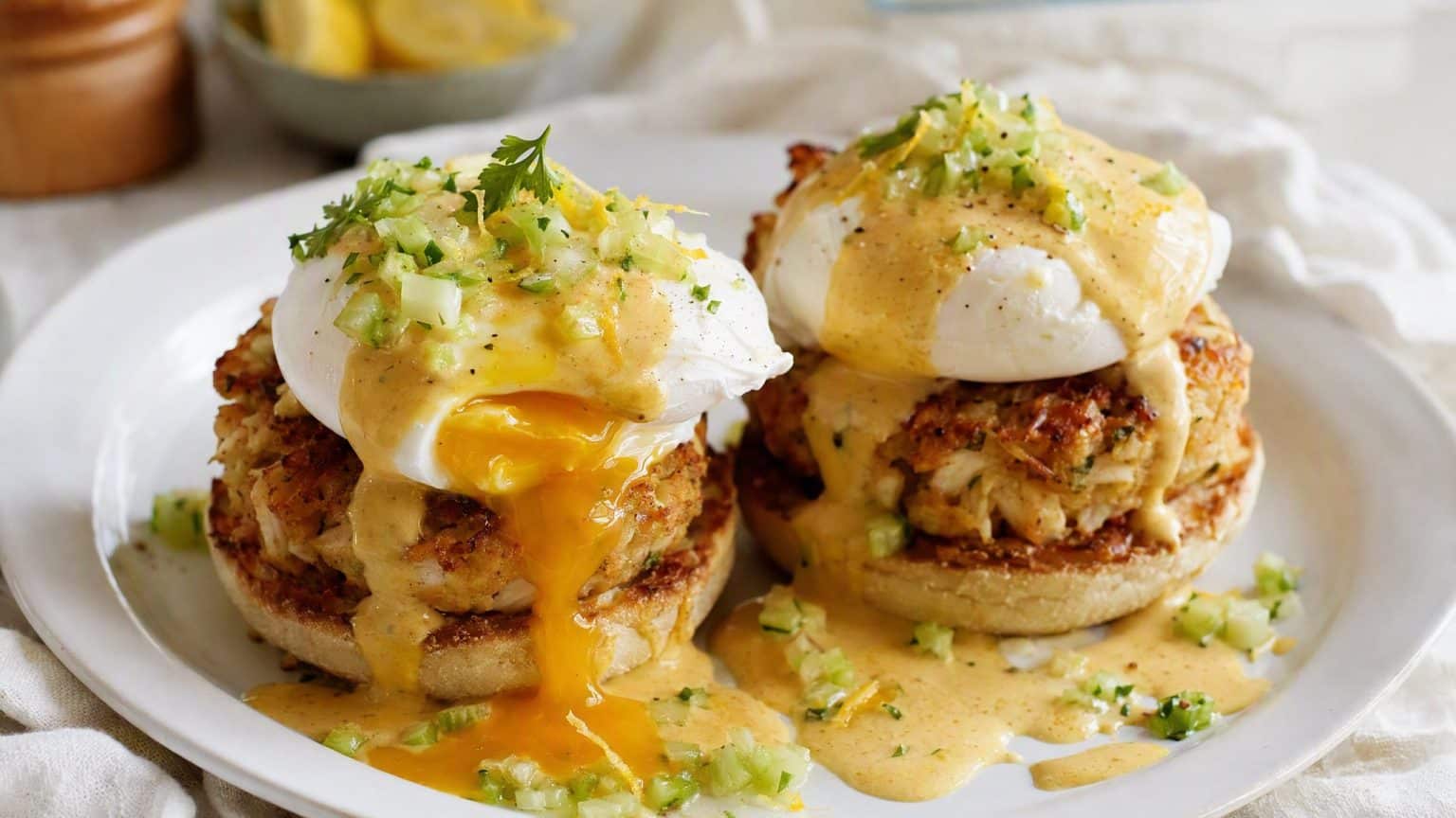 Crab cakes on a split toasted muffin topped with poached eggs, one yolk running, nut-brown hollandaise pooling, with a bright celery-lemon relish scattered over.