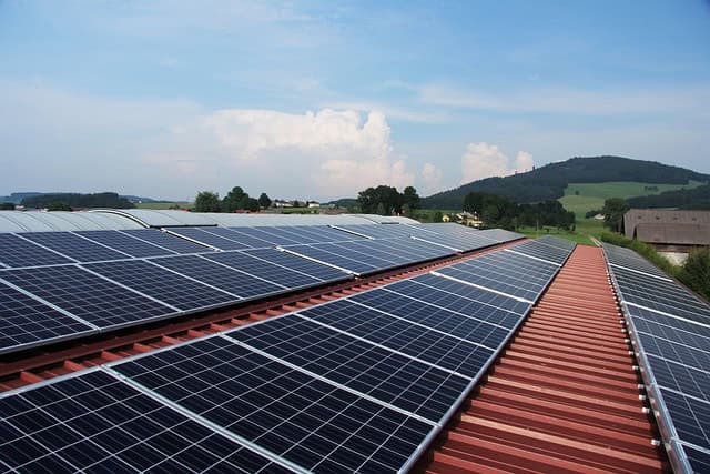 Solar panels on a red roof with a scenic background of hills and trees under a partly cloudy sky.