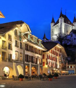 Rathausplatz (Town Hall Square) in Thun, Bern Canton, Switzerland at night, with the white keep of Thun Castle overlooking the scene