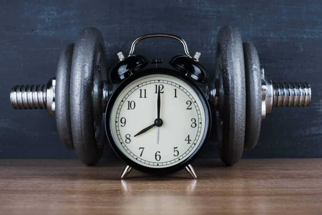 picture of a clock in front of dumbbells asking when is the best time to take creatine