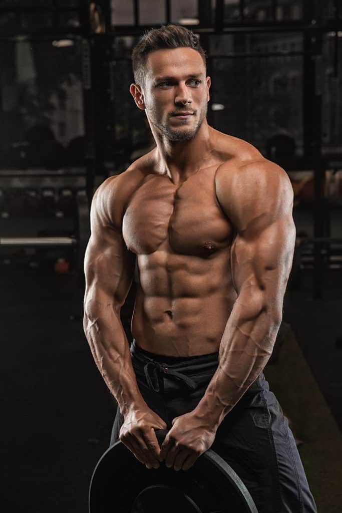 Young male bodybuilder with no shirt on holding a 45 pound plate in front of him