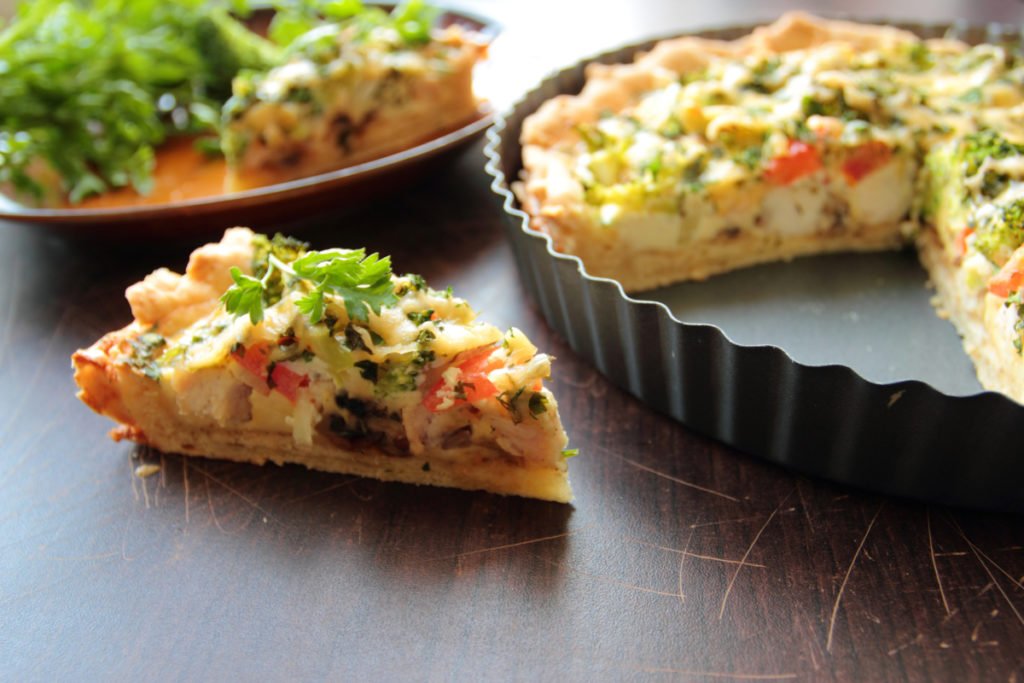 Picture of a quiche filled with shredded chicken, gruyere cheese, red peppers and onions