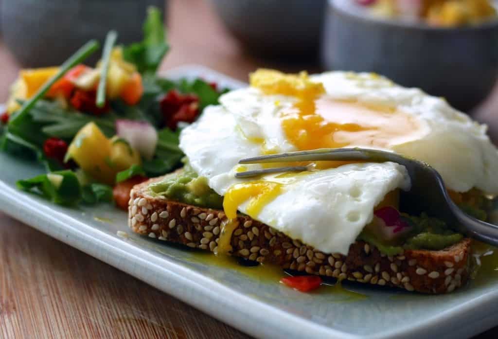 A picture of avocado toast with eggs sunny side up and a salad of greens, the perfect bodybuilding breakfast.