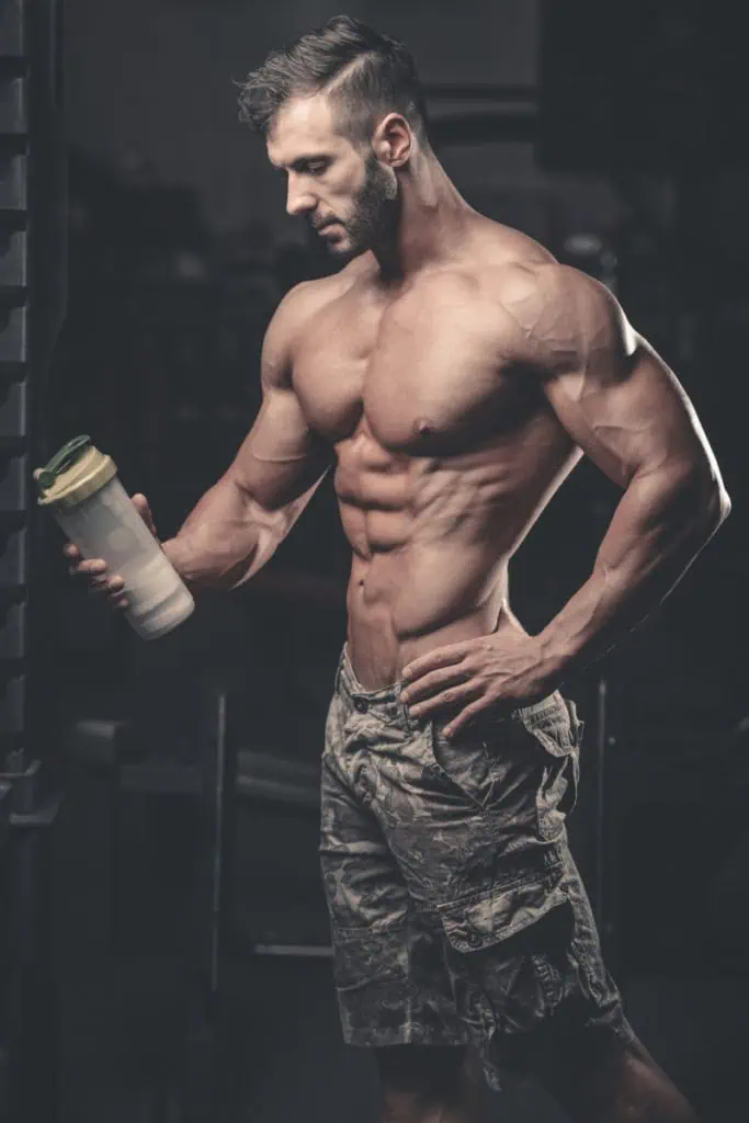 Muscular caucasian man on diet resting after exercise And drinking creatine monohydrate powder from shaker in the gym