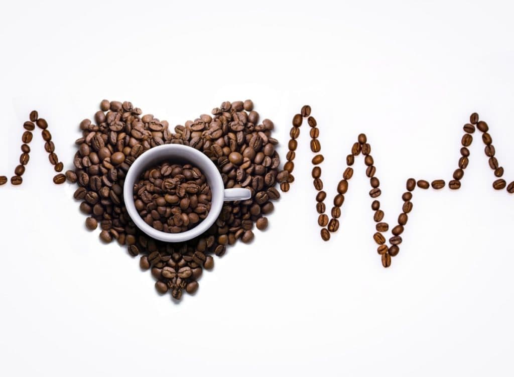 a picture of a heartbeat traced with coffee dicaffeine malate beans and in the center a pile of coffee anhydrous beans in the shape of a heart.