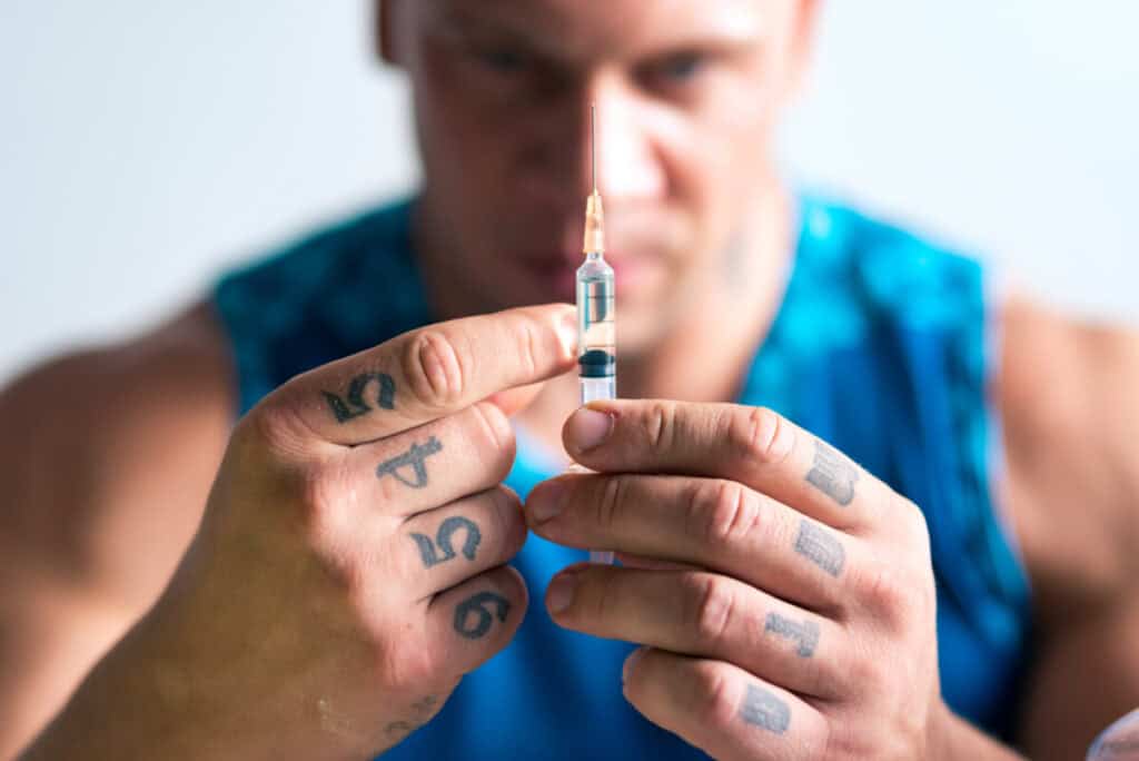 a male bodybuilder holding a syringe full of the illegal steroid anavar