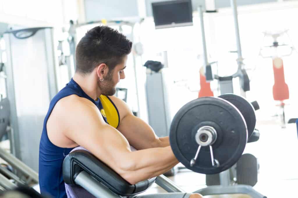 Handsome young man working out at the gym on a barbell curlbench