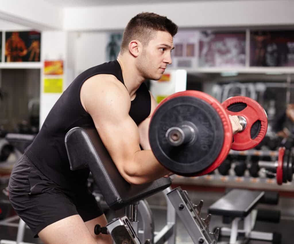 Young athletic man working his biceps at preacher curl bench at the gym