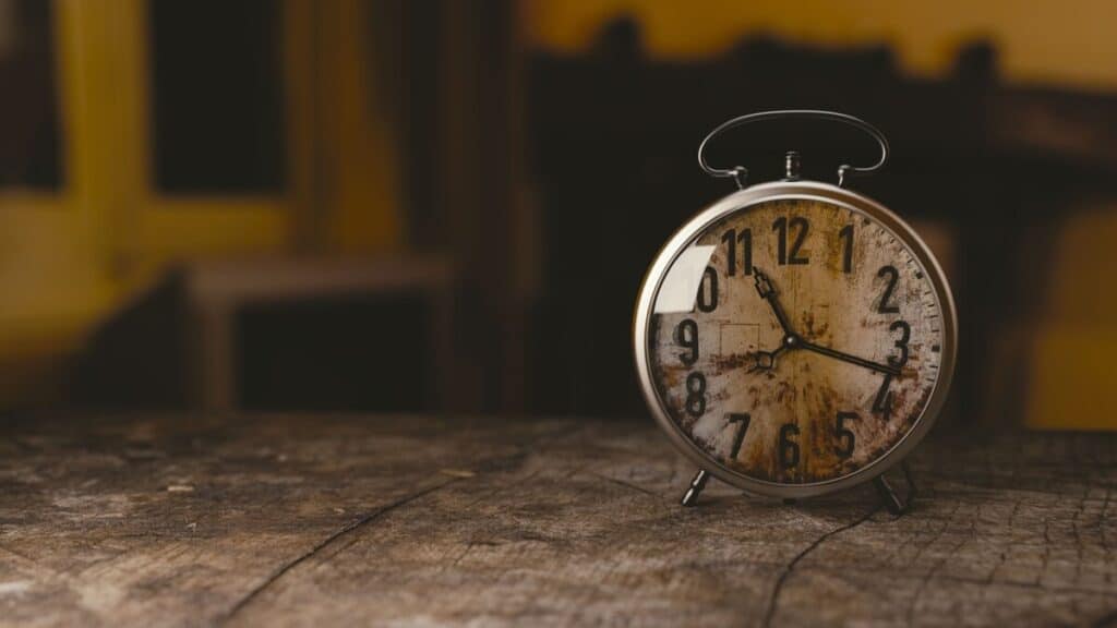 a wooden rustic table with an antiquec round clock sitting on it displaying 11:17 as the time