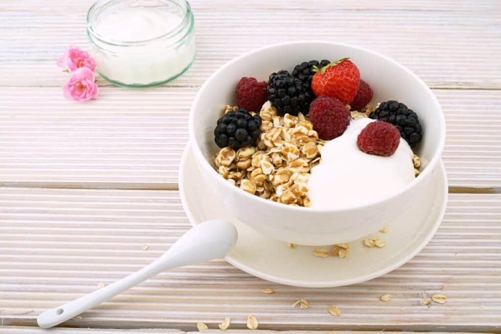 A white bowl with granola, raspberries, and blackberries. Sitting on a white picnic table.