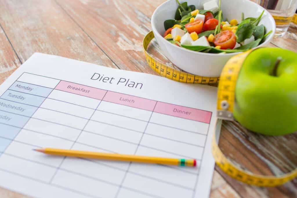 healthy eating, thermogenic diet plan slimming and weigh loss concept - close up of diet plan paper green apple, measuring tape and salad