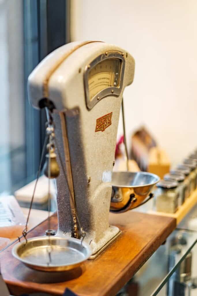 An antique scale with 2 pendulums sitting on a wooden table.