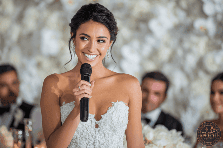 A bride in a strapless white wedding dress smiles while holding a microphone, with guests seated and blurred in the background.