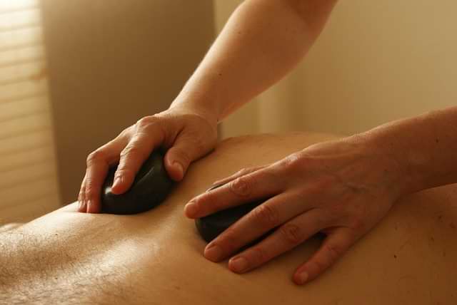 Hands glide warm basalt stones across a back—serene hot stone massage.