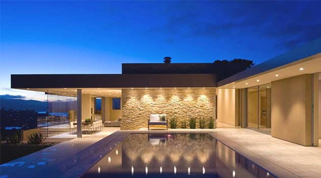 Modern luxury house exterior with a heated pool, sleek architecture, and ambient lighting at twilight, showcasing contemporary design and elegant outdoor living space.