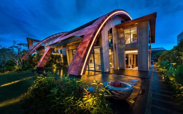 Futuristic modern house with curved architectural design, extensive glass windows, and lush landscaping, showcasing innovative architecture art, contemporary home design, and sustainable building concepts.