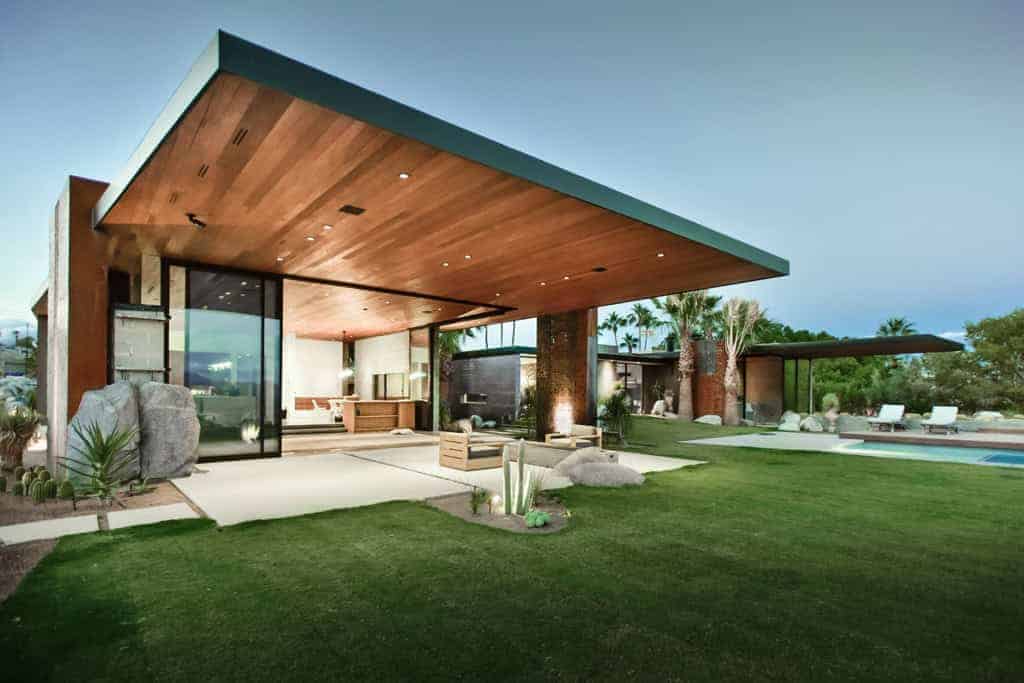 Modern luxury house with expansive glass walls, wooden accents, and a spacious backyard featuring a pool and lush landscaping, showcasing contemporary architectural design.