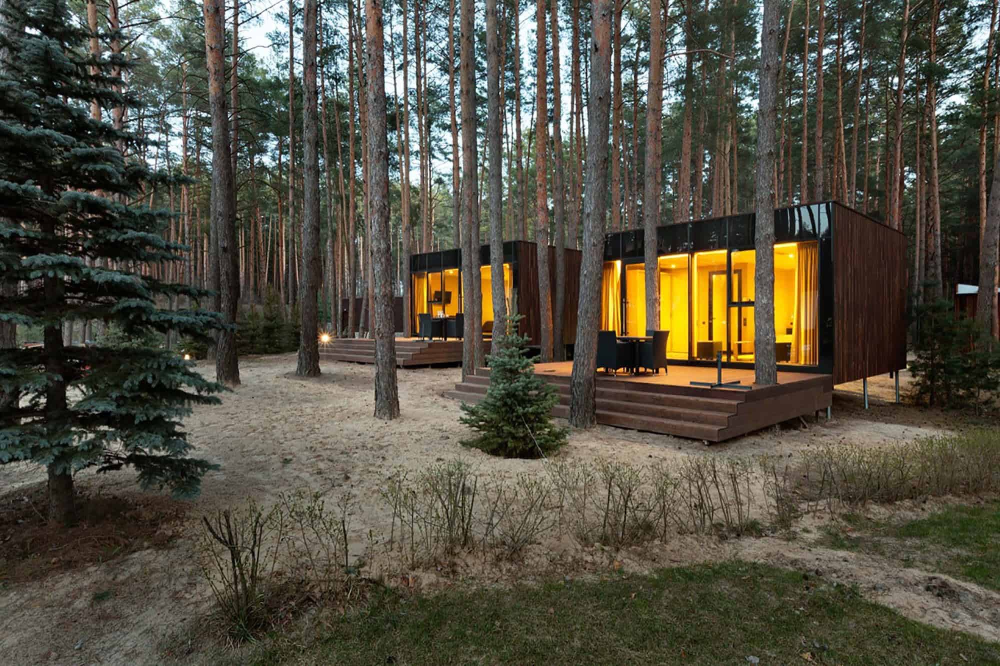 Modern forest luxury tiny homes with large glass windows and warm interior lighting, nestled among tall pine trees in a serene natural setting, blending contemporary architecture with nature.