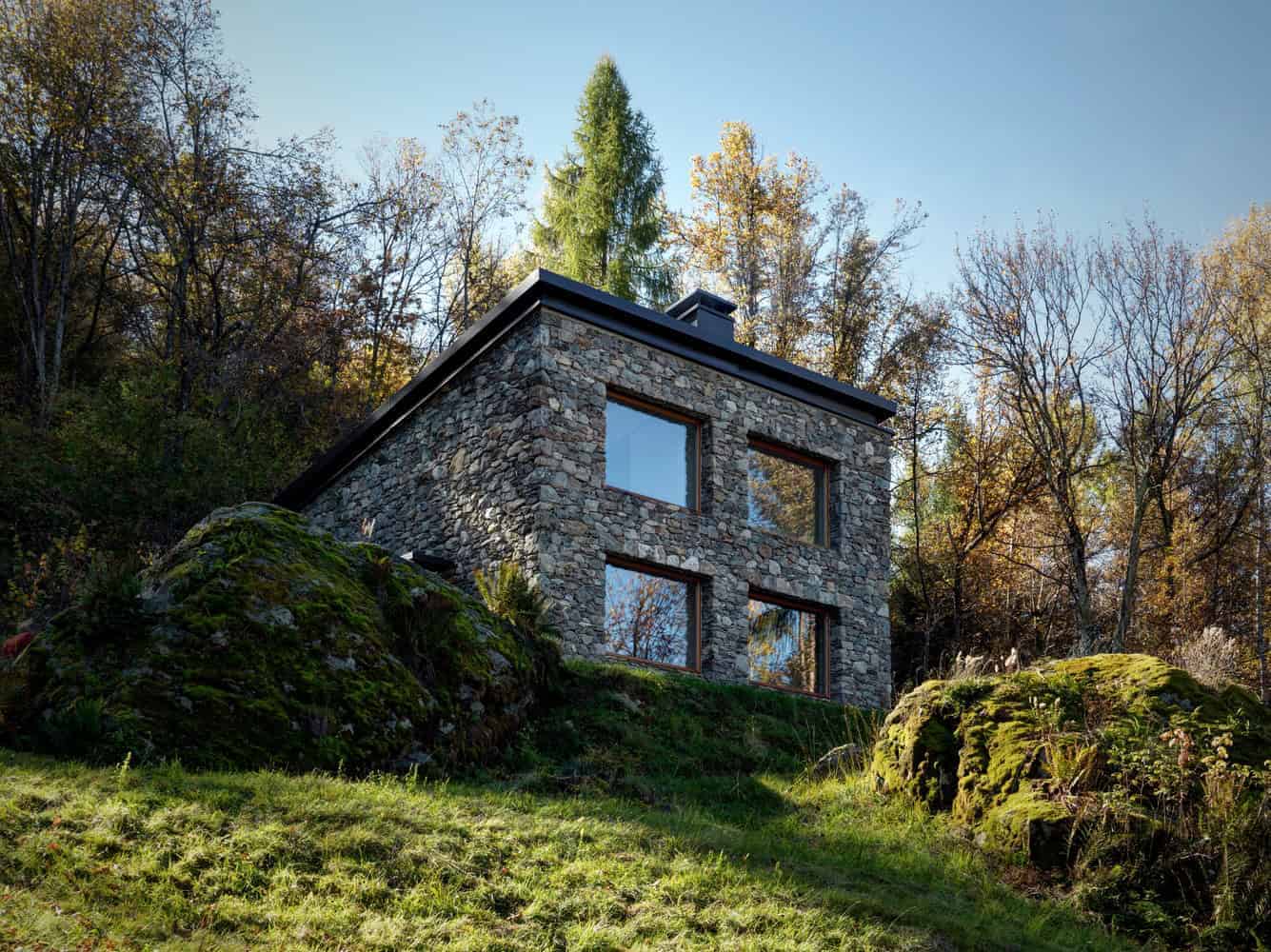 Luxury modern stone house built into a hillside surrounded by trees with large windows and contemporary design, showcasing innovative architecture and nature-inspired home design.